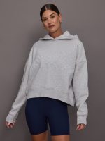 Woman wearing a gray hoodie and navy shorts against a gray background