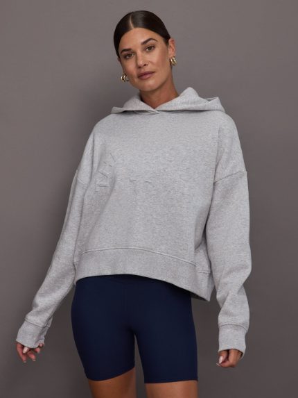 Woman wearing a gray hoodie and navy shorts against a gray background