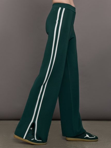 Model wears a pair of dark green track pants with white racer stripes down the sides.