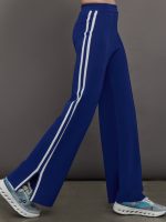 Model wears a bright blue pair of track pants with side slits at the ankles and white racing stripes down the sides.