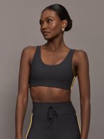 Model is wearing a black scoopneck sports bra with yellow striped sides.