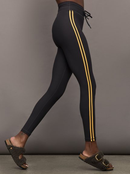Model is wearing black high waisted leggings with drawstring and yellow striped racing detail down sides. 