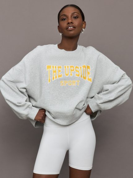 Model is wearing a light heather gray oversized sweatshirt with bold yellow lettering that says "The Upside Sport."