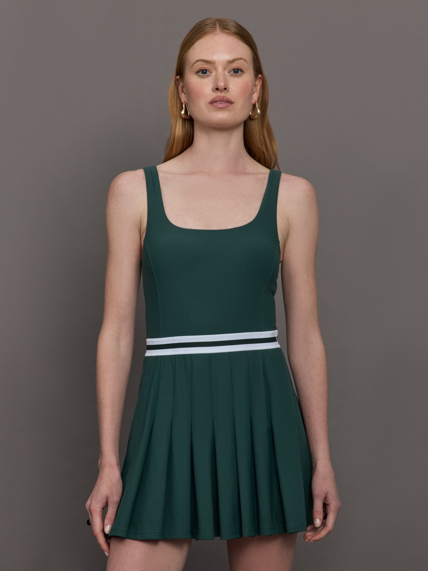 THEU-USW125120-GRNGRNDRK-Peached-Lucette-Pleated-Dress-color-Green_13648-Edit Model wears a dark green wide scoop neck tennis dress with pleating and a white waistline.