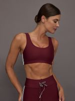Model wears a maroon sports bra and leggings against a gray background