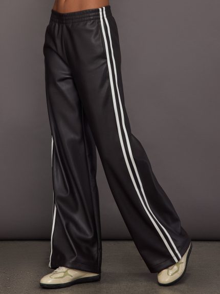 Model wears a pair of dark brown vegan leather track pants with white stipes down side.