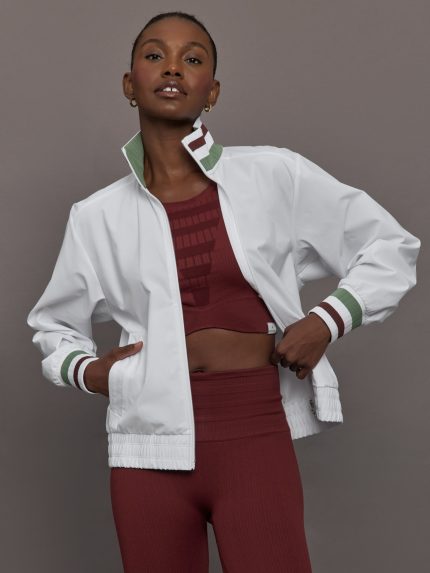 Model wears white track jacket with a high collar, front zipper, and ribbed cuffs and hem.